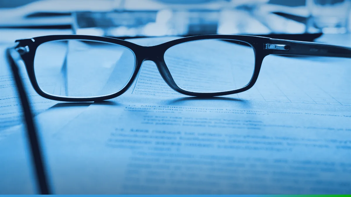 Óculos de leitura apoiados sobre um documento impresso em uma mesa clara.