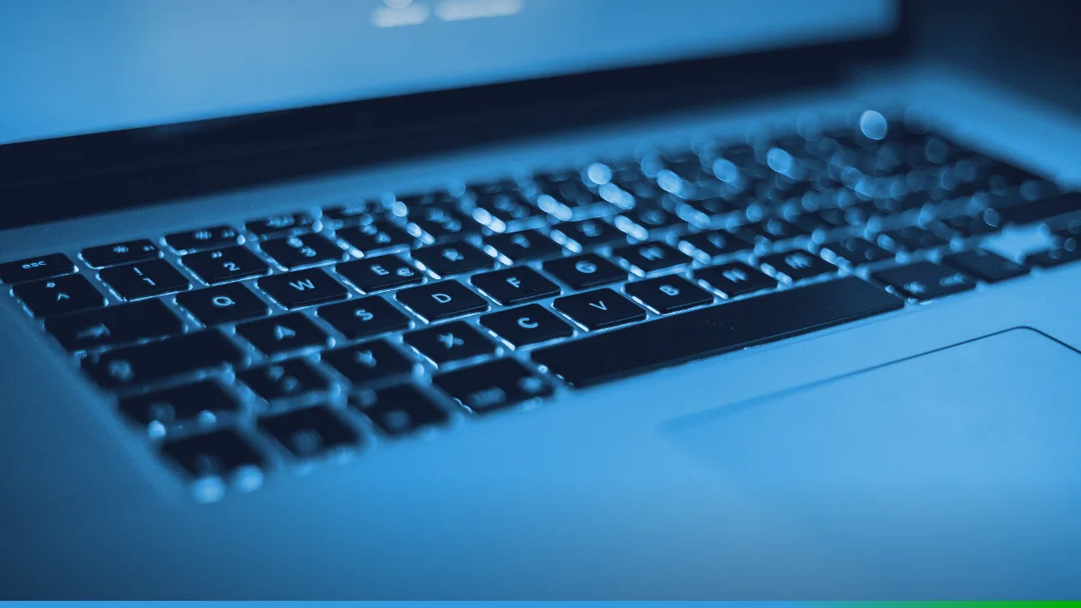 PW Host - Hospedagem de Sites Vitalícia e Sem Mensalidade Teclado iluminado de um notebook visto de perto, com a tela desfocada ao fundo.