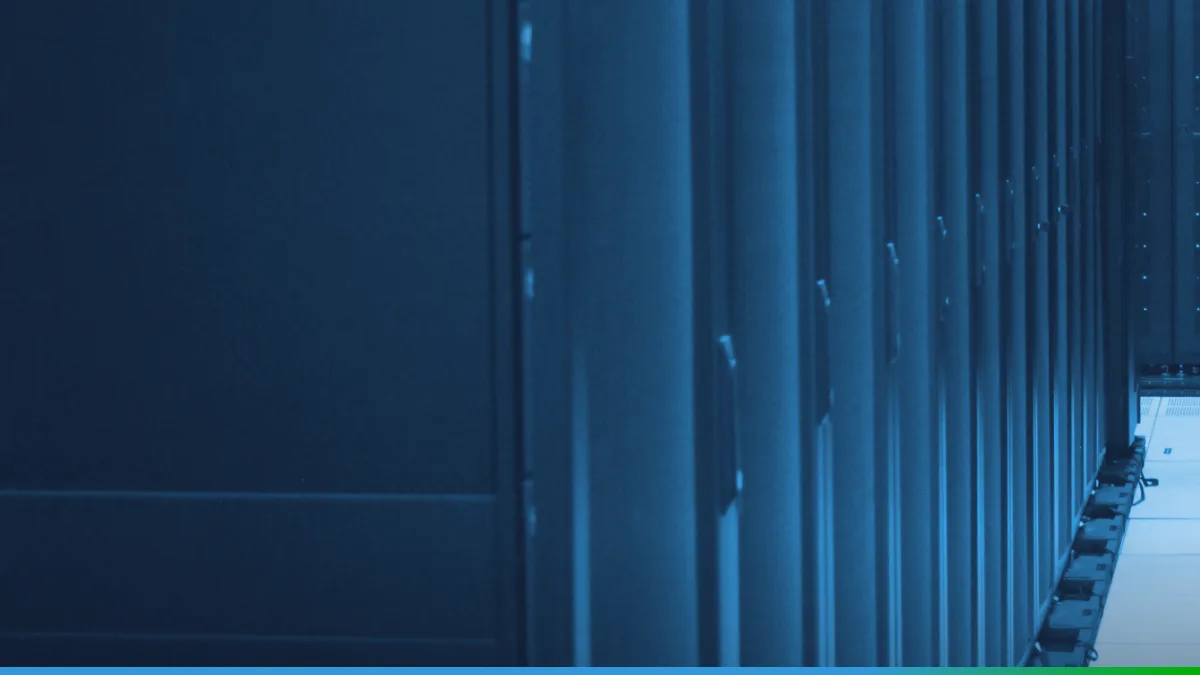 Fileira de racks de servidores pretos num data center, vista de perto, com o piso claro do corredor à direita.